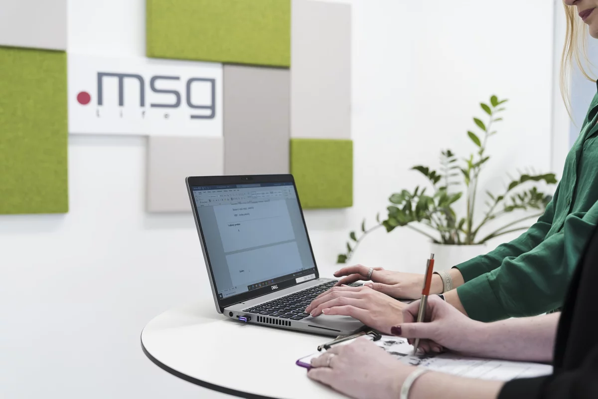 dva páry rúk pracujú na laptope a v píšu poznámky v msg kancelárii